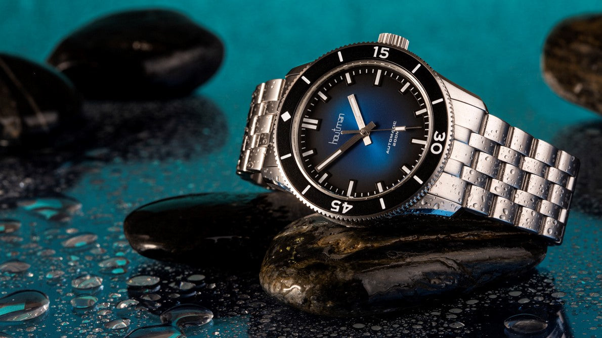 Blue dialled dive watch sits atop black river rock 
