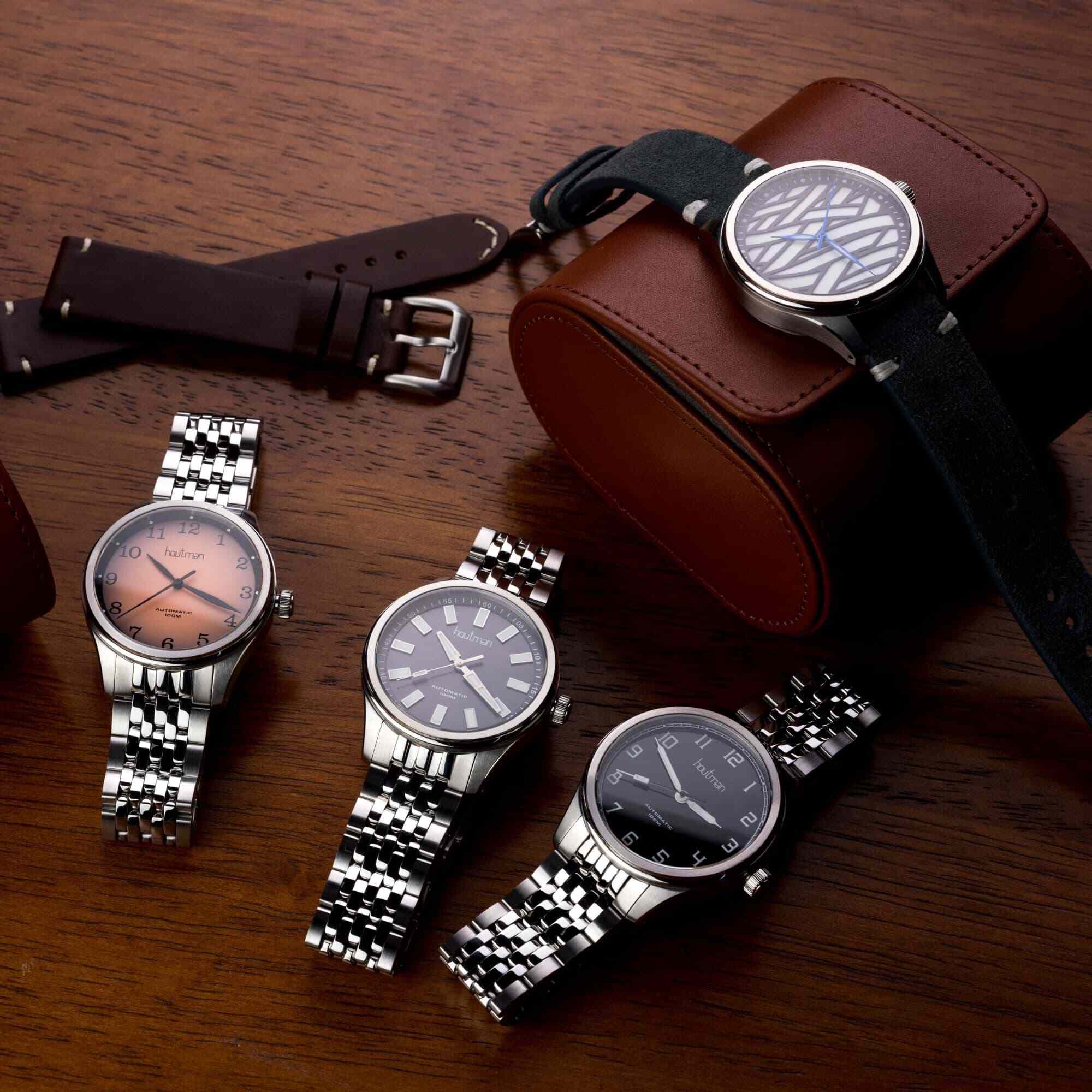 Swiss automatic watches on wooden desk. Australian watches one with salmon dial, one gloss black, one monochromatic and one grey dial.